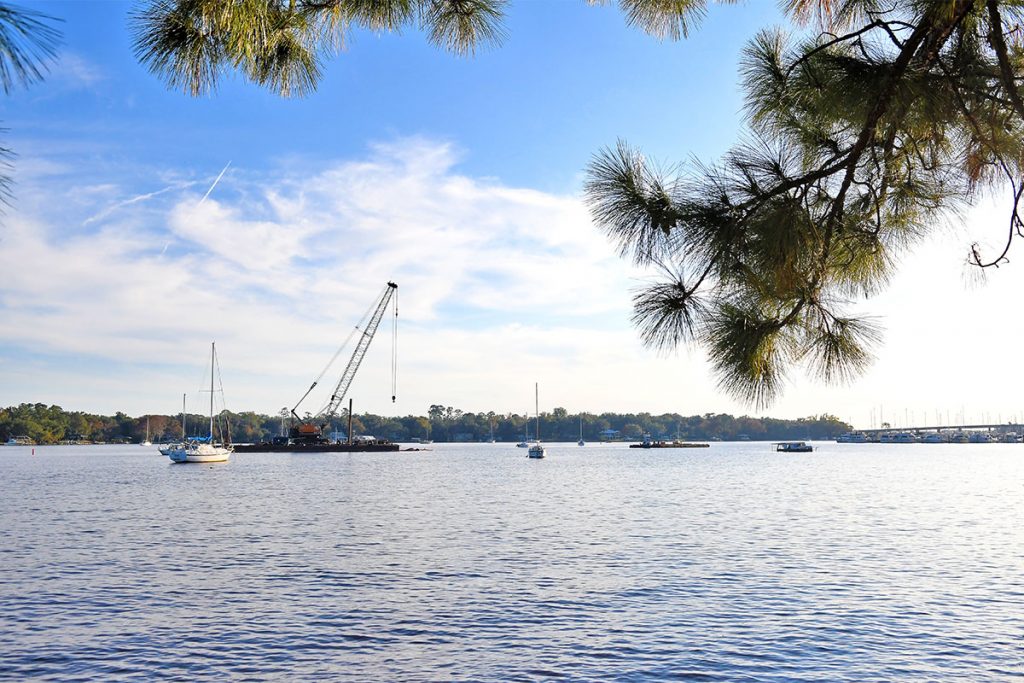 A crane is shown removing a derelict houseboat and floating structure near Stinson Park in Ortega.