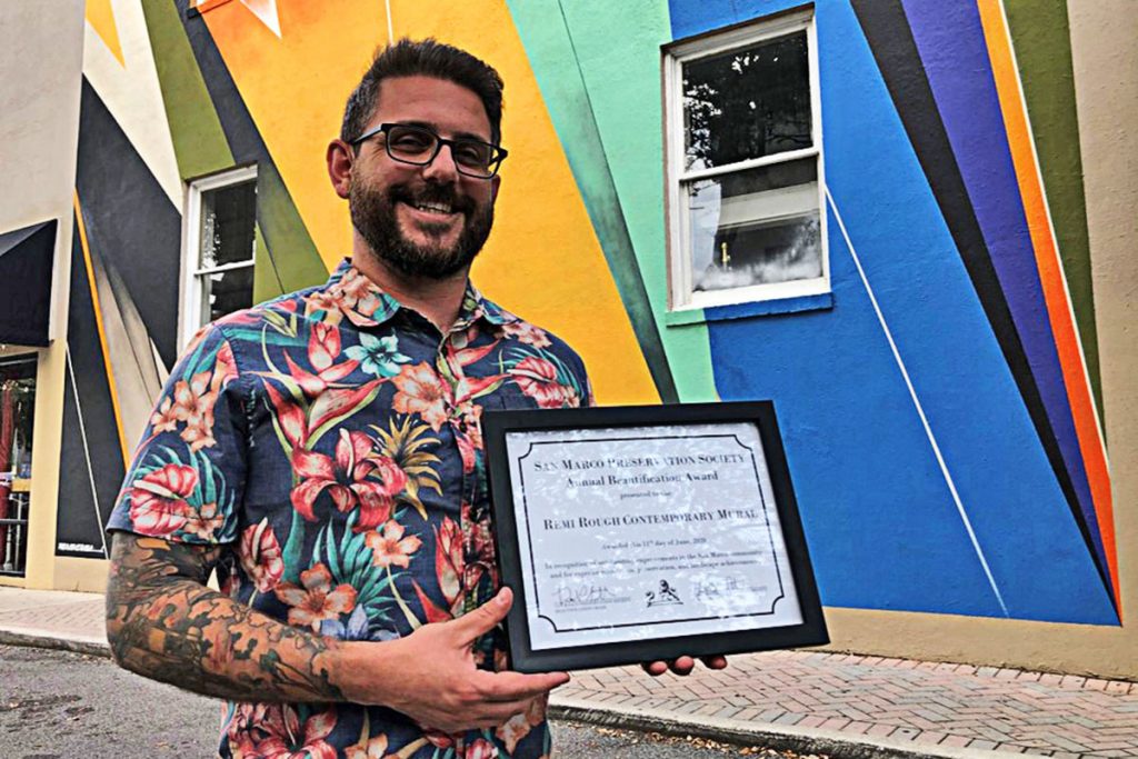 Miles Howard holds the SMPS beautification award for the mural on the wall of Grape and Grain