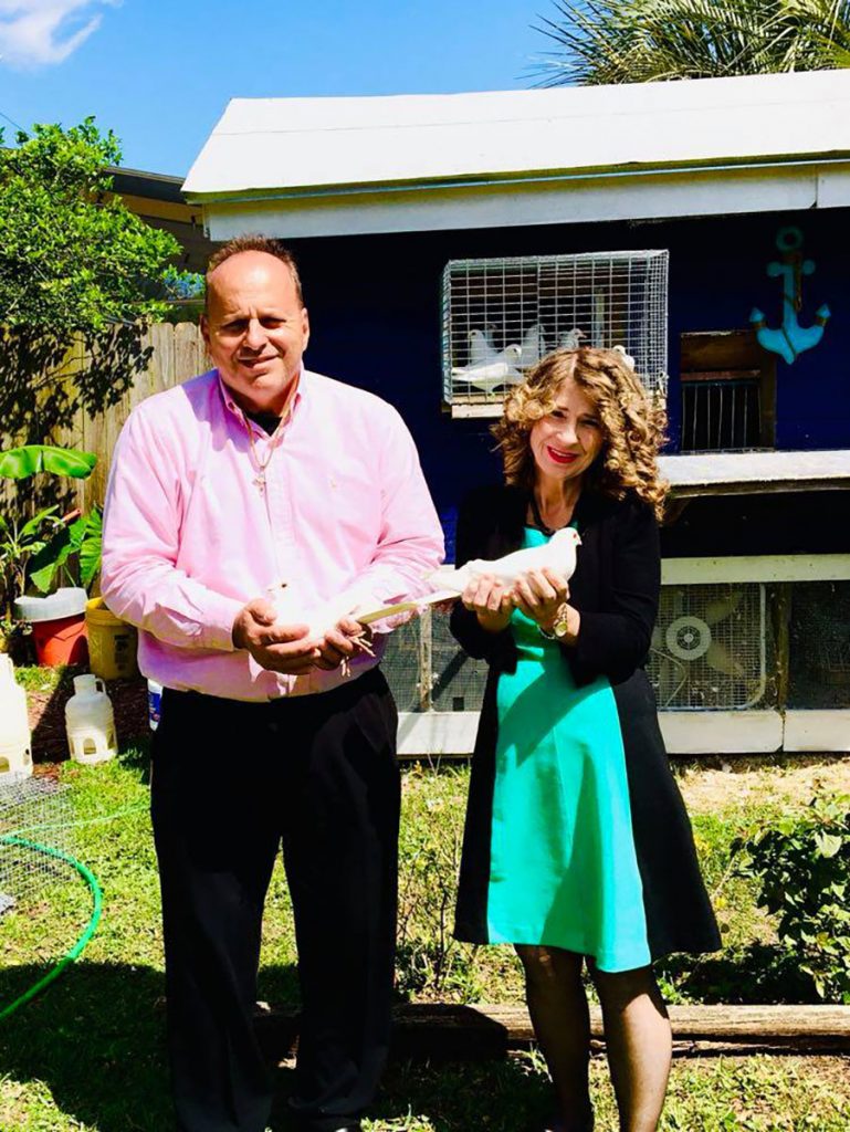 Mike & Carolyn Pirrone holding their ceremonial white birds in front of one of their lofts.n front of their home loft.