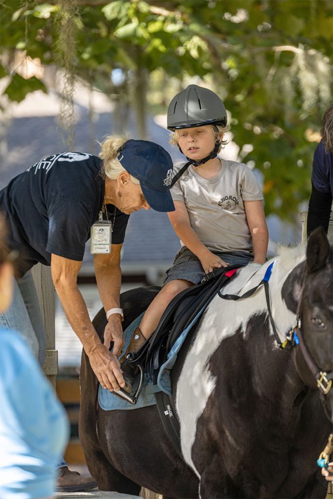 Volunteer Cathy Gurick adjusts rider Ozzie’s stirrup on Radical.