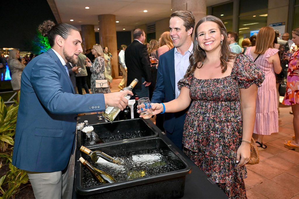 man serving drinks to smiling man and woman