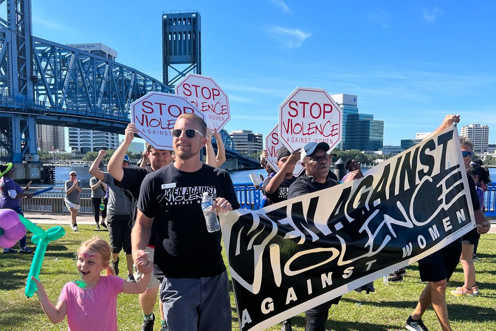 people carrying signs that say "Stop violence against women" and a banner that says "Men against violence against women"