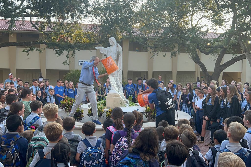 large crowd of kids around statue with man pouring bucket onto statue pedestal