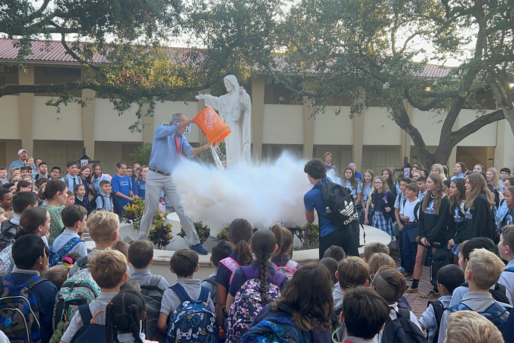 large crowd of kids around statue with man pouring bucket onto statue pedestal