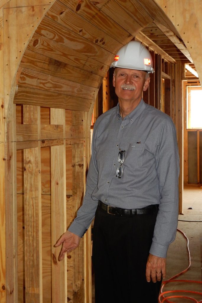 man standing under unfinished arched hall framing work