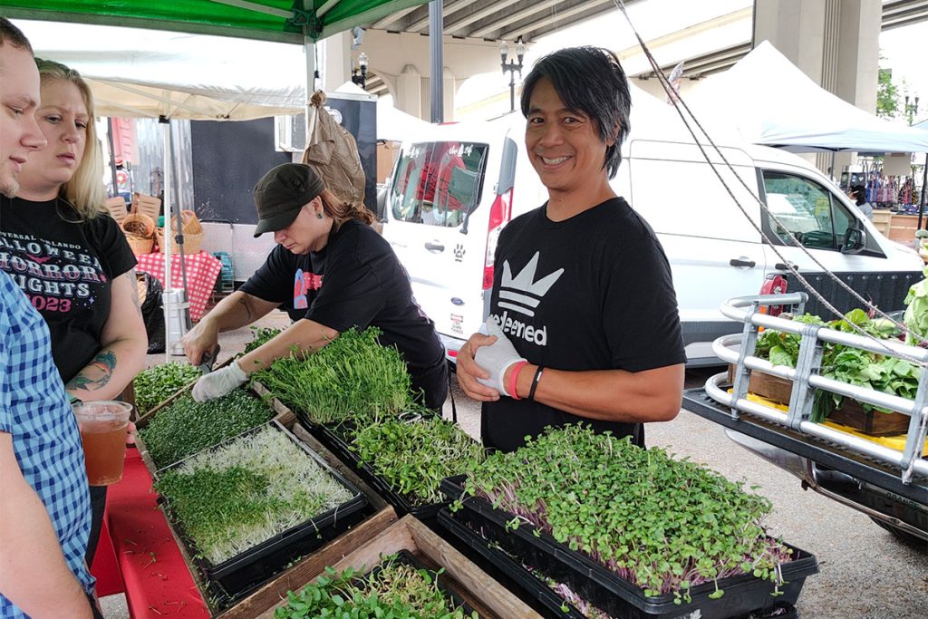 Dave Misola smiling with flowers and vegetables on display and Krystal Misola tending to vegetables and people looking over displayed items