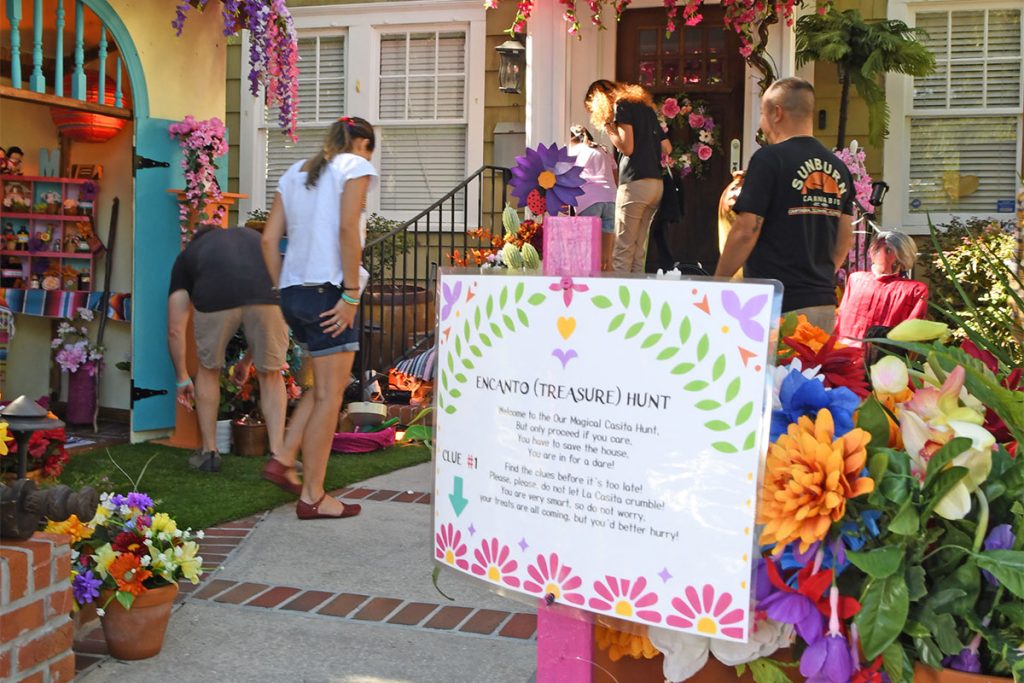 bright colors and people looking around. Sign that says "Encanto (Treasure) Hunt with instructions.