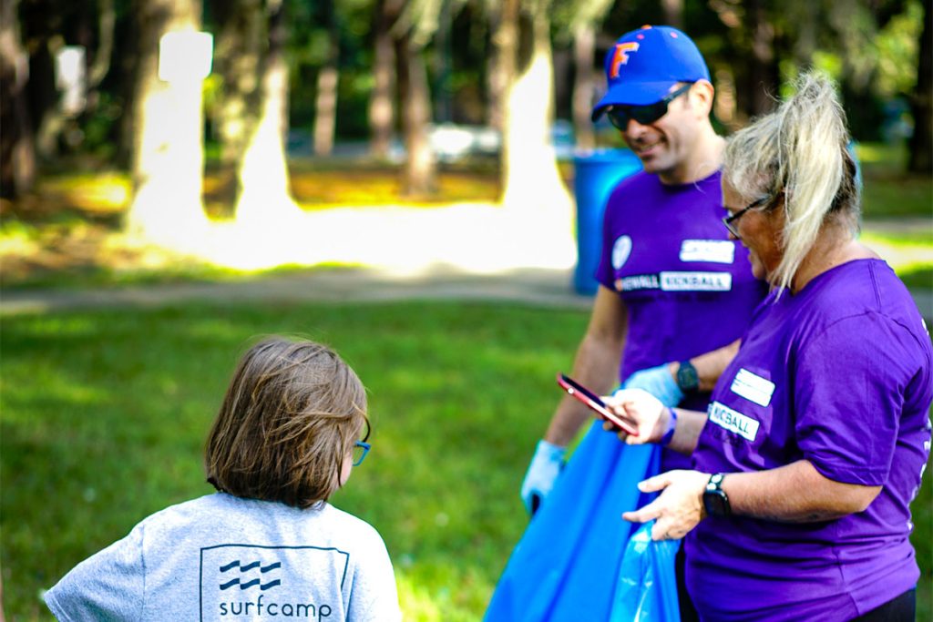 man and woman smiling as girl uses tool to place trash into trash bag
