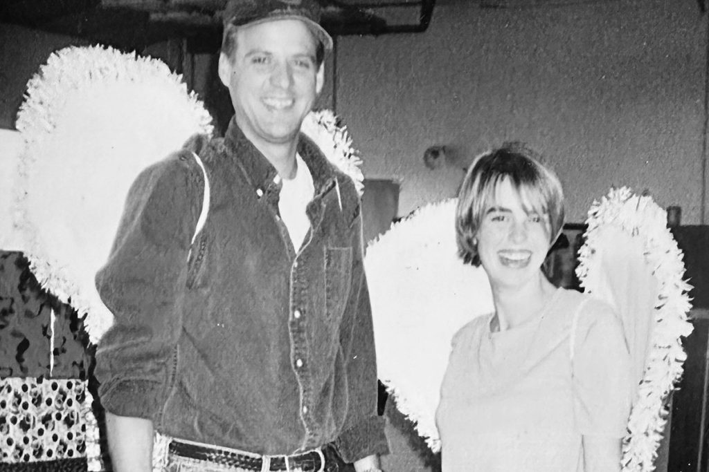 black and white photo of younger Leigh & Bryan smiling and wearing angel wings