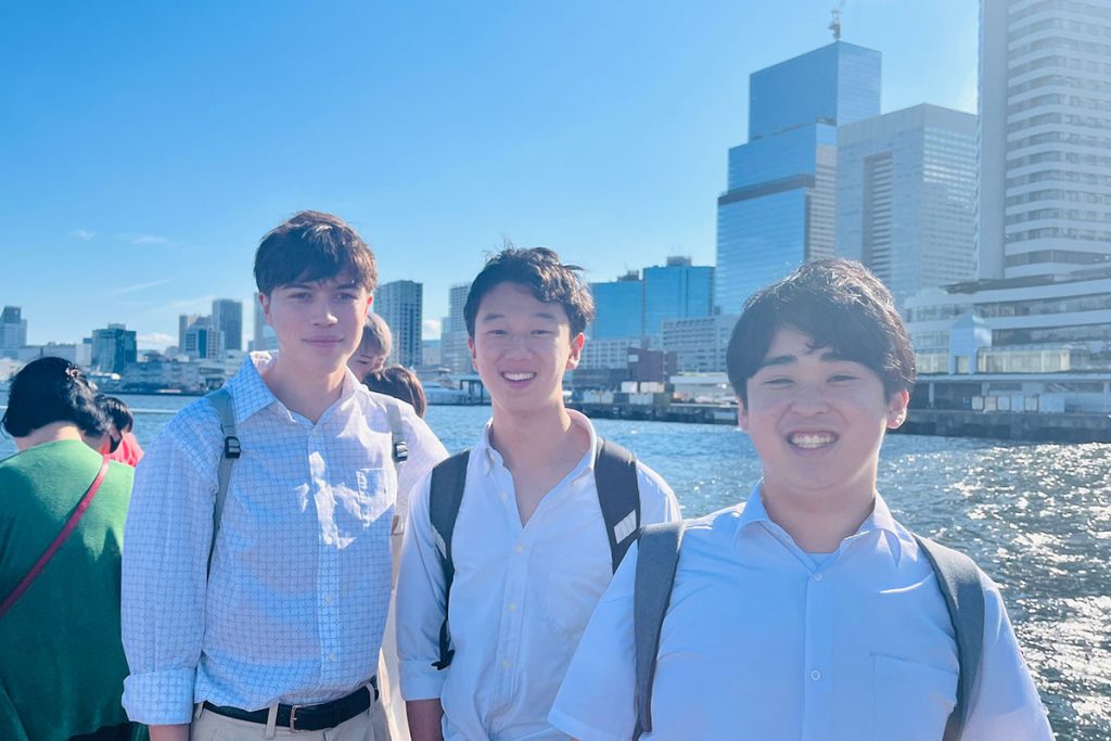 3 male students in Japan smiling, with city buildings in background across water