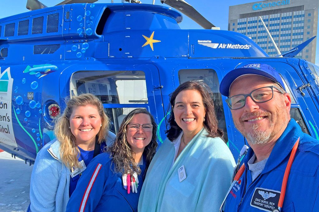 Ashley Helmick, executive director of the Women's Board with Kids Care Mobile ICU Team Member Cortni Sant CCT RN, Kendra McCrary, president of the Women's Board and Craig Skirvin CCT RRT in front of the Kids Kare helicopter. The Women's Board of Wolfson Children's Hospital is currently raising funds for this critical transport system.
